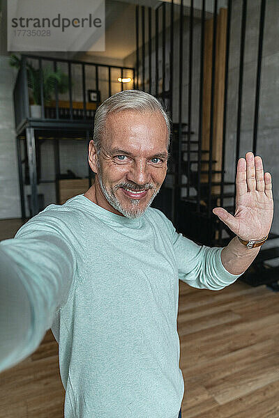 Lächelnder Mann gestikuliert und macht zu Hause ein Selfie