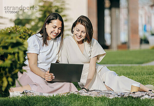 Fröhliche Freundinnen  die sich an einem sonnigen Tag im Park einen Laptop teilen