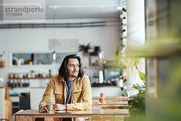 Hipster-Mann mit Kaffeetasse lehnt am Tisch im Café