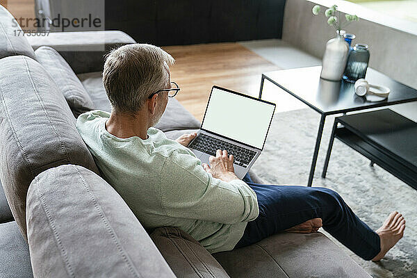 Geschäftsmann benutzt Laptop auf Sofa im Wohnzimmer zu Hause