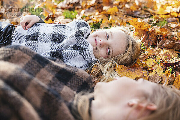 Smiling girl looking at mother lying on autumn leaves in park