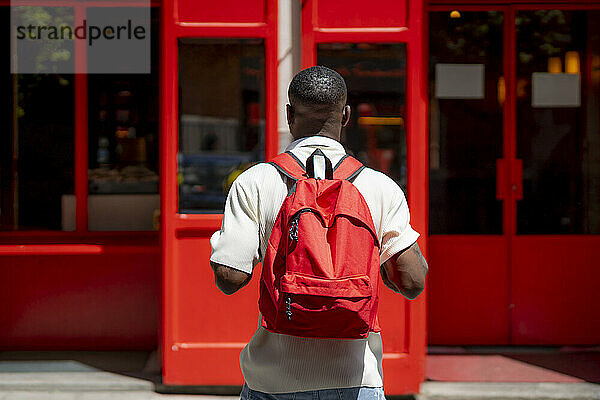 Mann steht an sonnigem Tag mit Rucksack vor rotem Gebäude