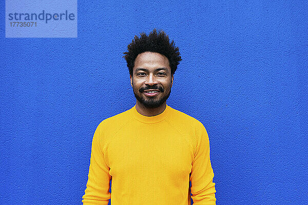 Lächelnder Afro-Mann steht vor blauer Wand