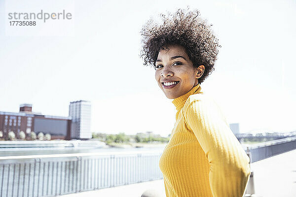 Glückliche Frau mit Afro-Frisur an der Promenade an einem sonnigen Tag