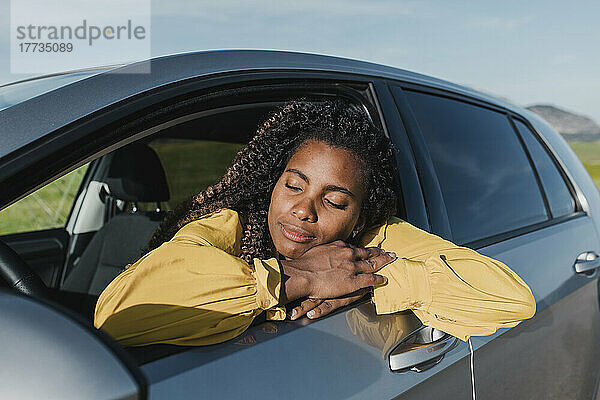 Frau mit geschlossenen Augen sitzt an einem sonnigen Tag im Auto