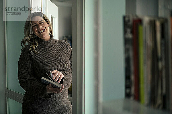 Glückliche Geschäftsfrau mit Buch steht vor der Tür im Büro