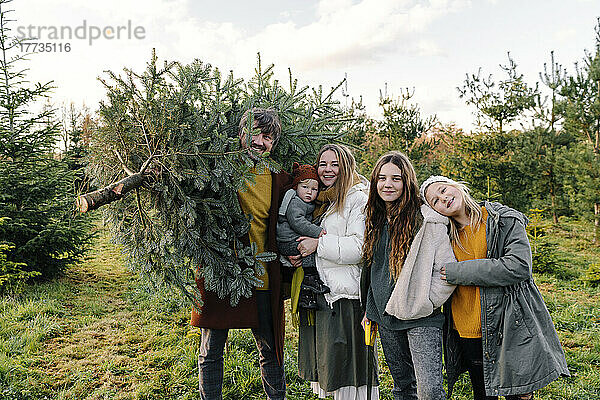 Glückliche Familie  die zusammen auf der Weihnachtsbaumfarm steht