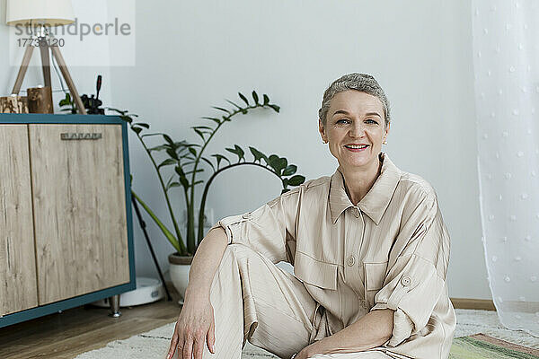 Porträt einer lächelnden reifen Frau  die zu Hause auf dem Boden sitzt