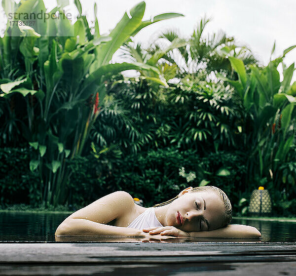Indonesia  Bali  Portrait of young woman leaning on edge of swimming pool