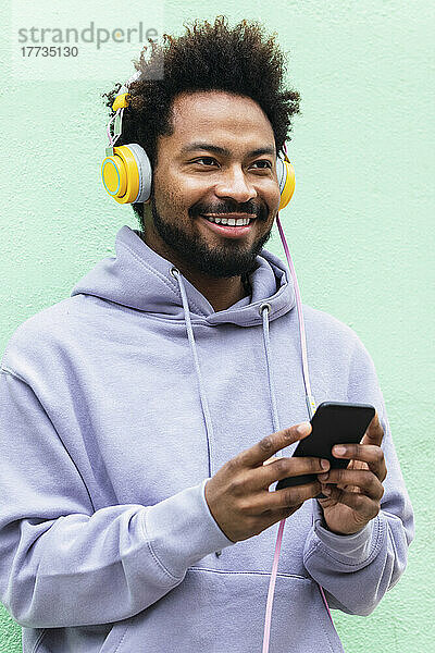 Lächelnder Mann hält sein Mobiltelefon in der Hand und hört Musik über Kopfhörer