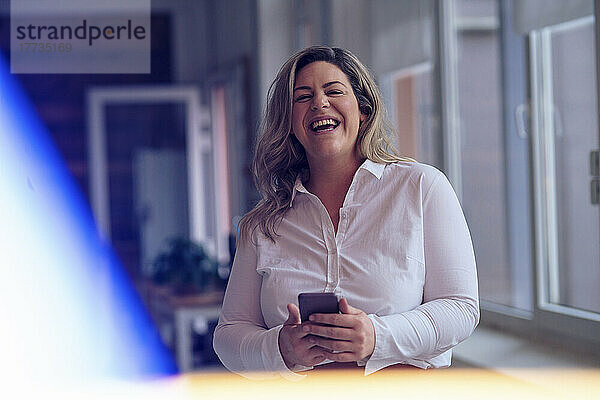 Cheerful businesswoman with mobile phone in office