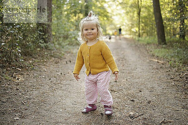 Smiling cute blond girl on footpath in forest