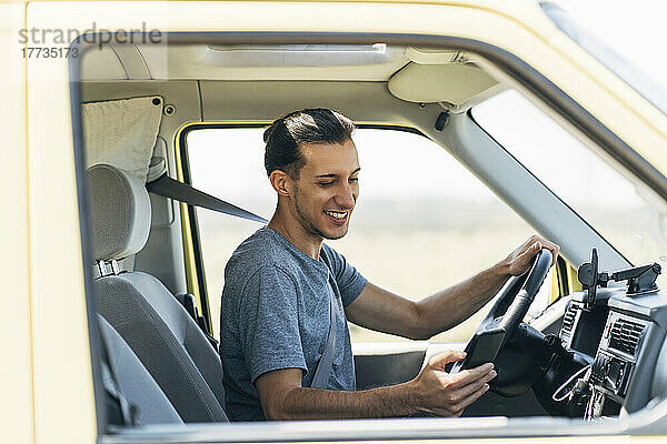 Lächelnder Mann  der im Lieferwagen sitzt und über sein Mobiltelefon im Internet surft