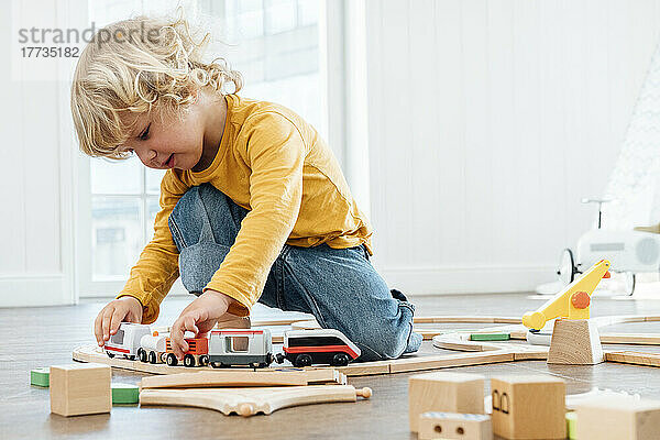 Netter Junge mit blonden Haaren  der zu Hause mit einer Spielzeugeisenbahn spielt