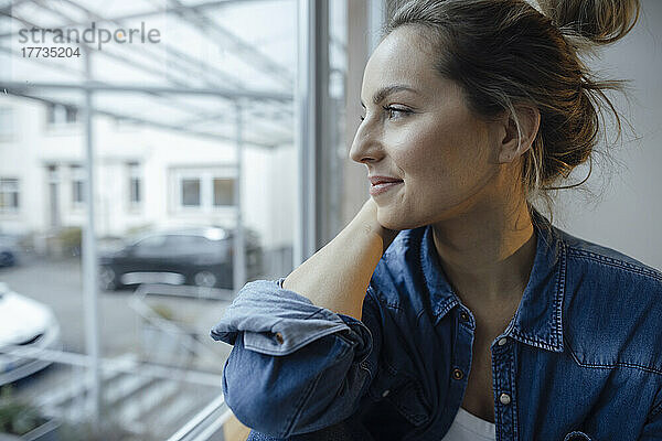 Thoughtful woman looking out through window at home