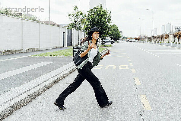 Junge Frau mit Smartphone überquert Straße