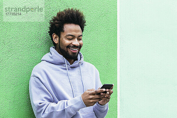 Glücklicher Mann benutzt Smartphone vor grüner Wand