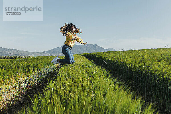 Lächelnde junge Frau springt auf grünes Gras