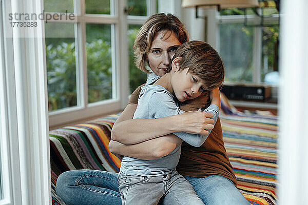 Reife Frau umarmt ihren Sohn  der zu Hause auf dem Sofa sitzt