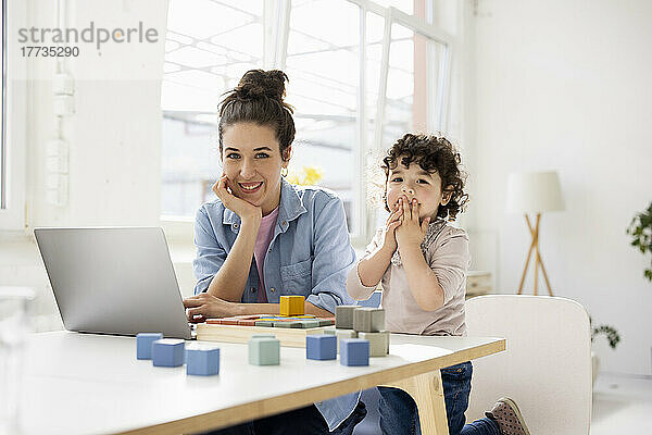 Mutter arbeitet von zu Hause aus mit Laptop  während Tochter mit Bauklötzen spielt