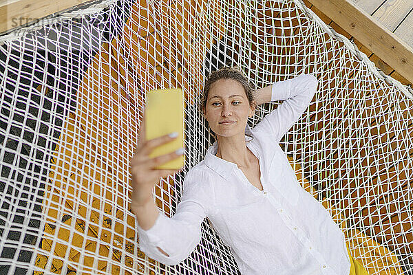 Frau macht Selfie mit Smartphone und liegt auf Hängematte
