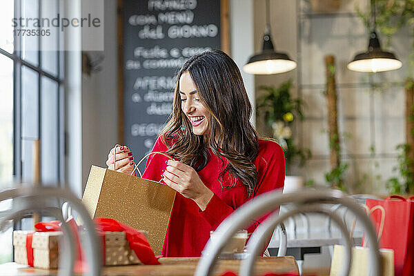 Fröhliche junge Frau schaut im Café nach einer Einkaufstasche