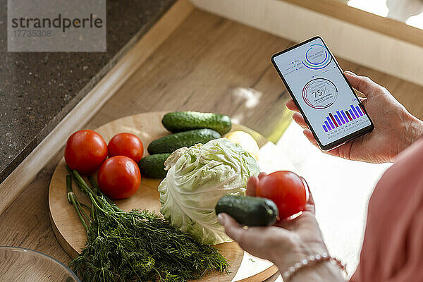 Frau hält Smartphone mit mobiler App und Gemüse