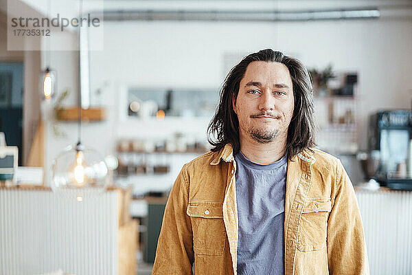 Lächelnder Hipster-Mann mit langen Haaren steht im Café