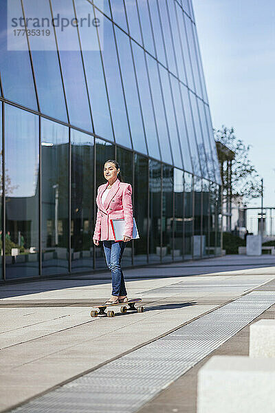 Reife Geschäftsfrau beim Skateboarden durch modernes Bürogebäude