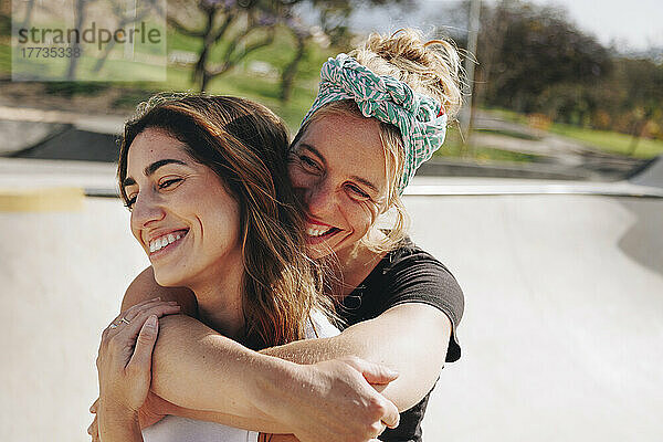 Lächelnde Frau umarmt ihre Freundin an einem sonnigen Tag von hinten