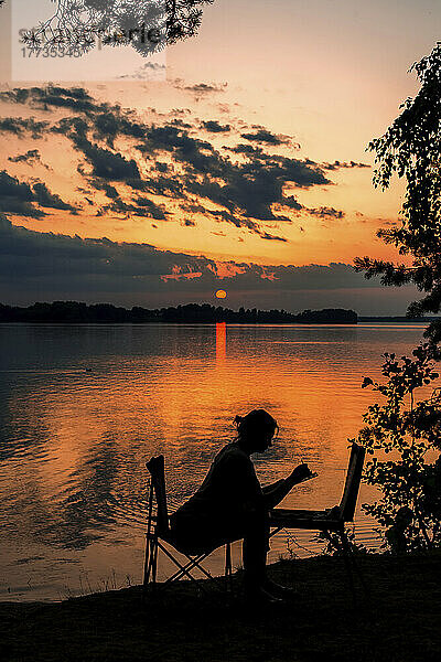 Silhouette einer Frau malt am See bei Sonnenuntergang