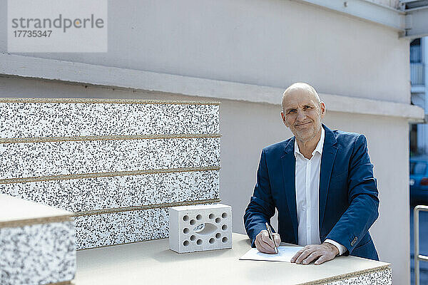 Lächelnder leitender Architekt mit Dokument durch Betonziegel auf der Baustelle
