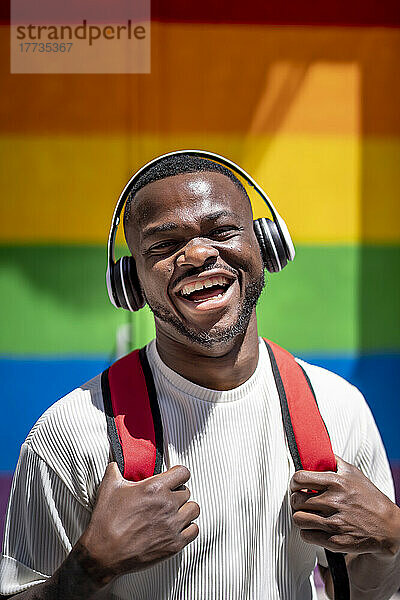 Fröhlicher junger Mann  der an einem sonnigen Tag Musik über kabellose Kopfhörer hört