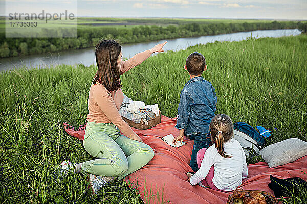 Junge Frau neben Kindern  die auf Fluss und Feld zeigen