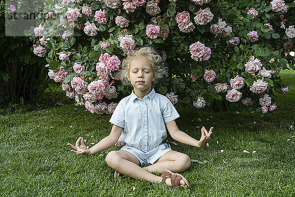 Mädchen mit geschlossenen Augen meditiert im Gras im Rosengarten