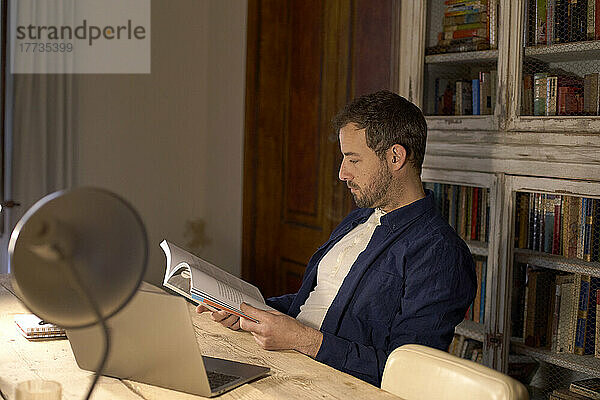 Geschäftsmann liest Buch am Schreibtisch im Heimbüro