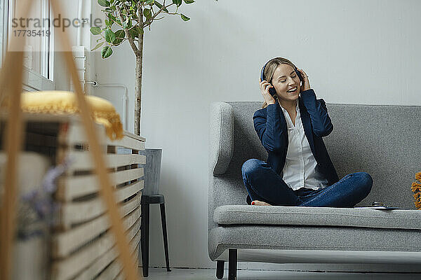 Glückliche Geschäftsfrau  die auf dem Sofa im Büro Musik über kabellose Kopfhörer hört