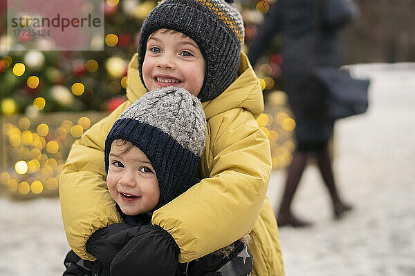 Lächelnde Brüder umarmen sich auf dem Weihnachtsmarkt