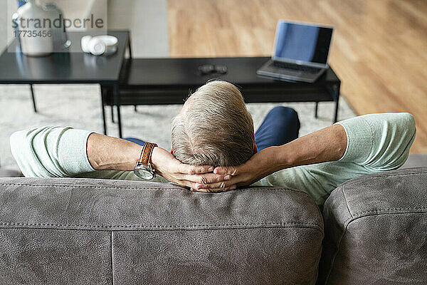 Man with hands behind head sitting on sofa at home