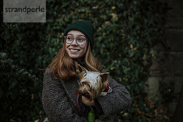 Glückliche Frau mit Strickmütze und Yorkshire Terrier im Park