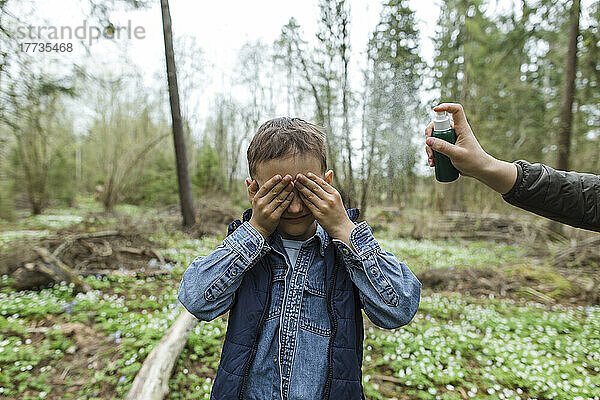 Mutter sprüht Insektenschutzmittel auf Sohn  der ihm im Wald die Augen zuhält
