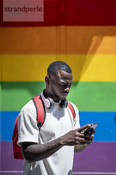 Junger Mann benutzt Smartphone vor Regenbogenwand
