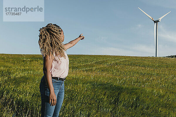 Junge Frau zeigt auf eine Windmühle  die auf einer Wiese steht