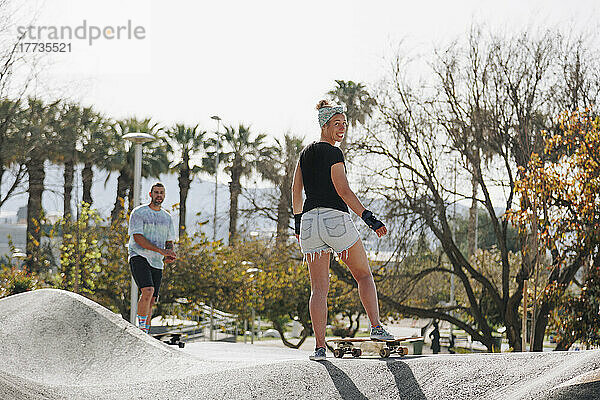 Lächelnde Frau mit Skateboard vor Freund auf Sportrampe
