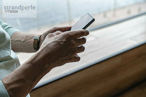 Hände eines Mannes  der zu Hause sein Smartphone am Fenster benutzt