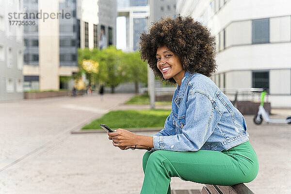 Glückliche Afro-Frau mit Mobiltelefon sitzt auf Bank