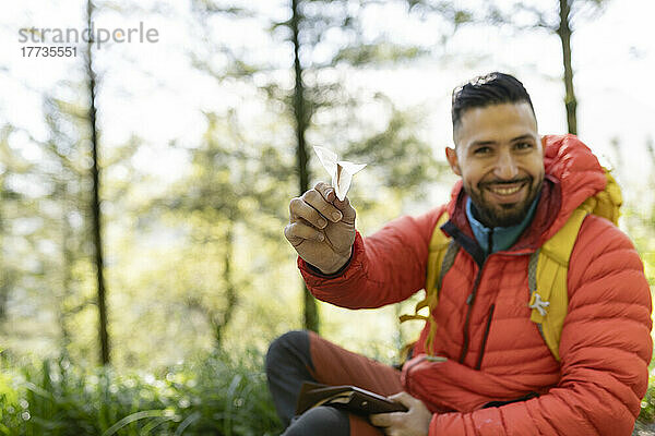 Lächelnder Wanderer mit Papierflieger sitzt im Wald