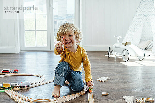 Glücklicher Junge  der zu Hause mit einer Spielzeugeisenbahn sitzt