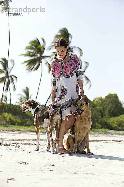 Frau streichelt Hunde am Strand