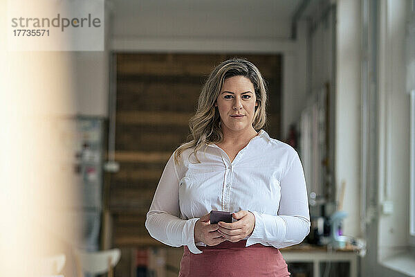 Selbstbewusste Geschäftsfrau in Übergröße mit Mobiltelefon im Büro